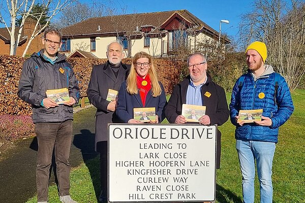 Five Exeter Lib Dems with canvassing cards stand in front of a road sign for Oriole Drive